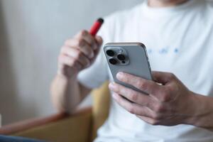 Kyiv, Ucrânia - pode 2, 2024. vermelho descartável eletrônico cigarro com Iphone 15 dentro uma do homem mão. moderno conectados comunicação foto