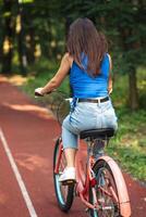 mulher equitação bicicleta em estrada dentro a verão parque ao ar livre, costas Visão foto