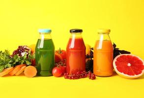 garrafas com suco saudável, frutas e vegetais na cor de fundo foto