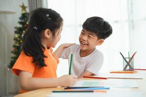 dois crianças estão sentado às uma mesa com giz de cera e coloração livros. elas estão sorridente e rindo, desfrutando seus Tempo junto. conceito do felicidade e amizade entre a dois crianças foto