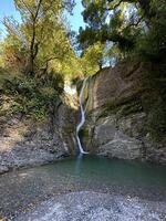 uma tranquilo cascata fluxos para dentro uma claro como cristal lagoa cercado de exuberante vegetação e rochoso penhascos, evocando Paz e natural beleza foto