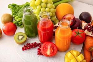 garrafas com sucos saudáveis, frutas e vegetais em fundo claro