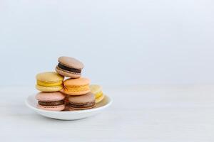 saboroso francês macarons em uma branco placa. branco de madeira fundo, pastel cores. foto