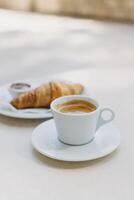 copo do Preto café e uma croissant em uma mesa dentro uma rua cafeteria. foto