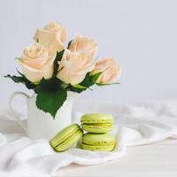 dois luz verde francês macarons com concurso rosas dentro uma vaso em branco fundo. fechar acima. pistache macarons. foto