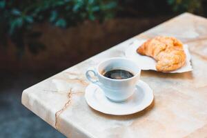 copo do café e uma croissant para café da manhã em uma mesa dentro uma rua cafeteria. foto