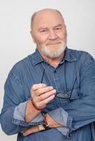 retrato do a atraente grisalho homem dentro uma jeans camisa isolado em uma cinzento fundo. barbudo avô do a europeu tipo. foto