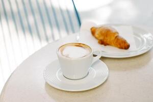 copo do cappuccino e uma croissant em uma mesa dentro uma rua cafeteria. seletivo foco. foto