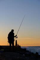 uma homem em pé e pescaria às a kyrenia Porto às a azul hora dentro Chipre foto