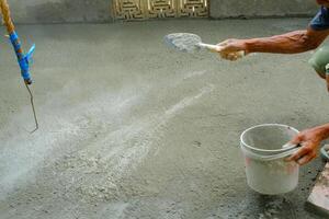 industrial fotografia. a mãos do uma pele escura trabalhador estão aspersão cimento pó para a fundida chão. aspersão cimento para endurecer a peças fundidas. foto