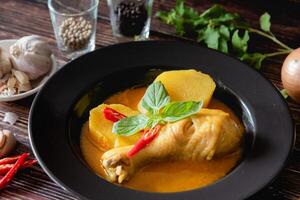 tradicional tailandês amarelo Curry com baqueta frango, fresco vegetal e erva dentro tigela em de madeira mesa, tailandês Comida conceito foto