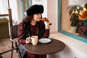 mulher dentro uma vermelho vestir é sentado às uma mesa com uma prato do Comida e uma copo do café. foto