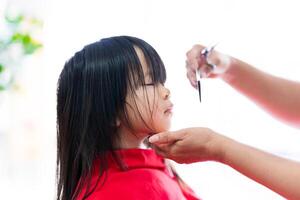 a mãos do uma barbeiro meticulosamente cortar a cabelo do uma fofa ásia garota. foto