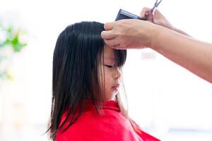 beleza salão estilo, mulher com tesouras e pente criando uma elegante Penteado. fechar-se uma pequeno criança menina corte dela cabelos de profissional barbeiros salão às barbeiro fazer compras. foto