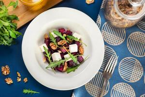 saudável salada com feta queijo, beterraba cubos, Rúcula, nozes, Oliva óleo, topo Visão plano deitar azul fundo foto