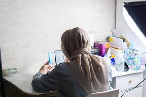 mulher com hijab é trabalhando com Móvel telefone para faço uma e produzir conteúdo para vendendo produtos foto