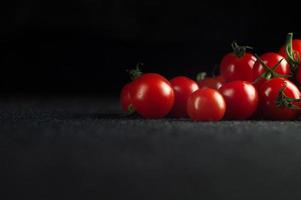 tomates cereja espalhados contra um fundo preto com um lugar vazio para uma inscrição. foto