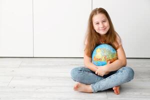 pequeno fofa menina sentado em a chão abraçando uma globo foto