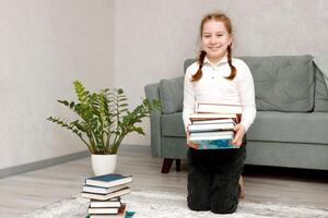 pequeno rindo menina com uma pilha do livros dentro dela mãos foto