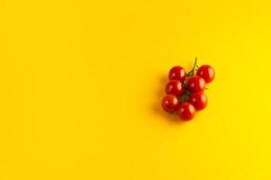 um raminho de tomate cereja em um fundo amarelo brilhante com um lugar vazio para uma inscrição. foto