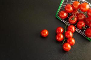 tomates cereja espalhados em uma cesta contra um fundo preto com um lugar vazio para uma inscrição. foto