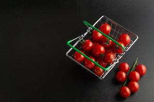 tomates cereja espalhados em uma cesta contra um fundo preto com um lugar vazio para uma inscrição. foto