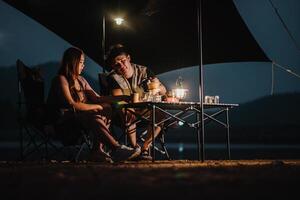 debaixo a noite céu, uma jovem casal ações uma momento sobre bebidas às seus iluminado acampamento, exalando uma acolhedor ambiente. foto