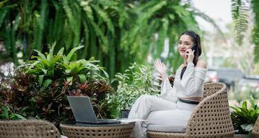 animado trabalhador autonomo tendo uma animado telefone conversação, confortavelmente sentado dentro a ao ar livre pátio configuração com vegetação em volta. foto