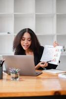 alegre empresária ações uma financeiro relatório, gesticulando positivamente para dela computador portátil dentro a escritório contexto. foto