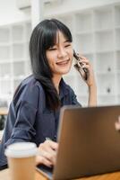 empresária com suspensórios sorrisos enquanto falando em a telefone, computador portátil aberto dentro frente do dela dentro uma brilhante escritório ambiente. foto