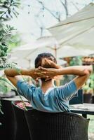 pessoa relaxa dentro uma jardim cadeira, mãos atrás cabeça, desfrutando uma pacífico ao ar livre contexto. foto