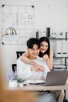 alegre jovem casal é visto desfrutando uma colaborativo momento dentro seus casa escritório, com uma foco em trabalho em equipe Como elas trabalhos em uma computador portátil. foto