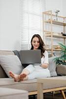 mulher dentro uma casual configuração confortavelmente navegando em dela computador portátil, com natural luz transmissão através a janela do dela arrumado vivo sala. foto