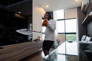 engraçado africano americano é limpeza casa fazendo tarefas domésticas limpeza chão com esfregão e ouvindo para música dentro sem fio fones de ouvido, africano americano homem é dançando e cantando foto