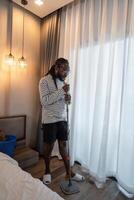 africano americano homem jovem limpar a chão com uma esfregão enquanto cantando dentro a quarto às casa foto