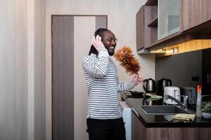 africano americano homem ouvindo para música enquanto limpeza dentro cozinha foto