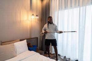 africano americano homem jovem limpar a chão com uma esfregão enquanto cantando dentro a quarto às casa foto