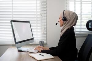 jovem muçulmano mulheres vestindo hijab telemarketing ou ligar Centro agente com fone de ouvido trabalhando em Apoio, suporte linha direta às escritório foto