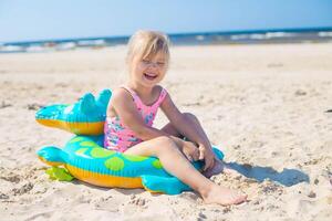 feliz menina do europeu aparência era do 5 sentado e rindo em a inflável crocodilo brinquedo às a de praia verão ensolarado dia.família verão vocação conceito. cópia de espaço. foto