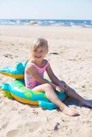 feliz menina do europeu aparência era do 5 sentado e rindo em a inflável crocodilo brinquedo às a de praia verão ensolarado dia.família verão vocação conceito. vertical foto. foto