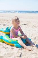 feliz menina do europeu aparência era do 5 sentado e rindo em a inflável crocodilo brinquedo às a de praia verão ensolarado dia.família verão vocação conceito. vertical foto. foto