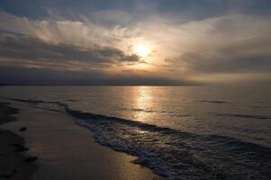 pôr do sol, iluminado mar. arenoso de praia dentro a primeiro plano. luz ondas. báltico mar foto