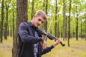 jovem macho toca violino no parque de verão foto