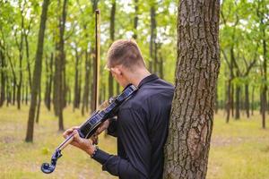 jovem macho toca violino no parque de verão foto