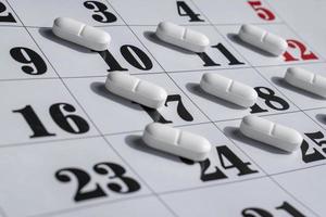 close-up de comprimidos brancos em um calendário. conceito de plano, cronograma, lista ou calendário de medicação. foto