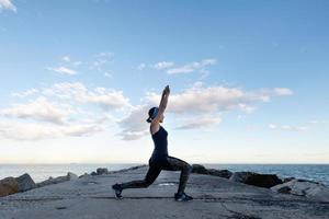mulher praticando ioga de frente para o mar em um dia nublado foto