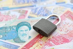 pequeno cadeado mentiras em pilha do iraniano dinheiro. sanções, banimento ou embargo conceito foto