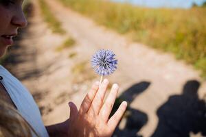 a menina detém dentro dela mãos uma azul flor do uma volta forma, uma esférico flor com muitos estames. uma variedade do flores silvestres. foto