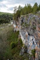 uma Alto penhasco a partir de a penhasco, a pedras estão coberto com musgo do vermelho cor, montanhoso terreno, lindo panorama dentro Rússia, a natureza do cedo primavera, fresco vegetação em a árvores foto