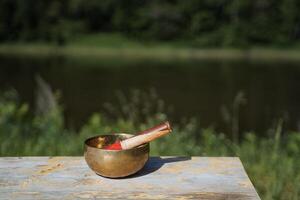 cobre cantando tibetano tigela com uma grudar, musical instrumento para meditação, sons do ioga cura, tigela em pé em a mesa, fundo natureza, zen foto